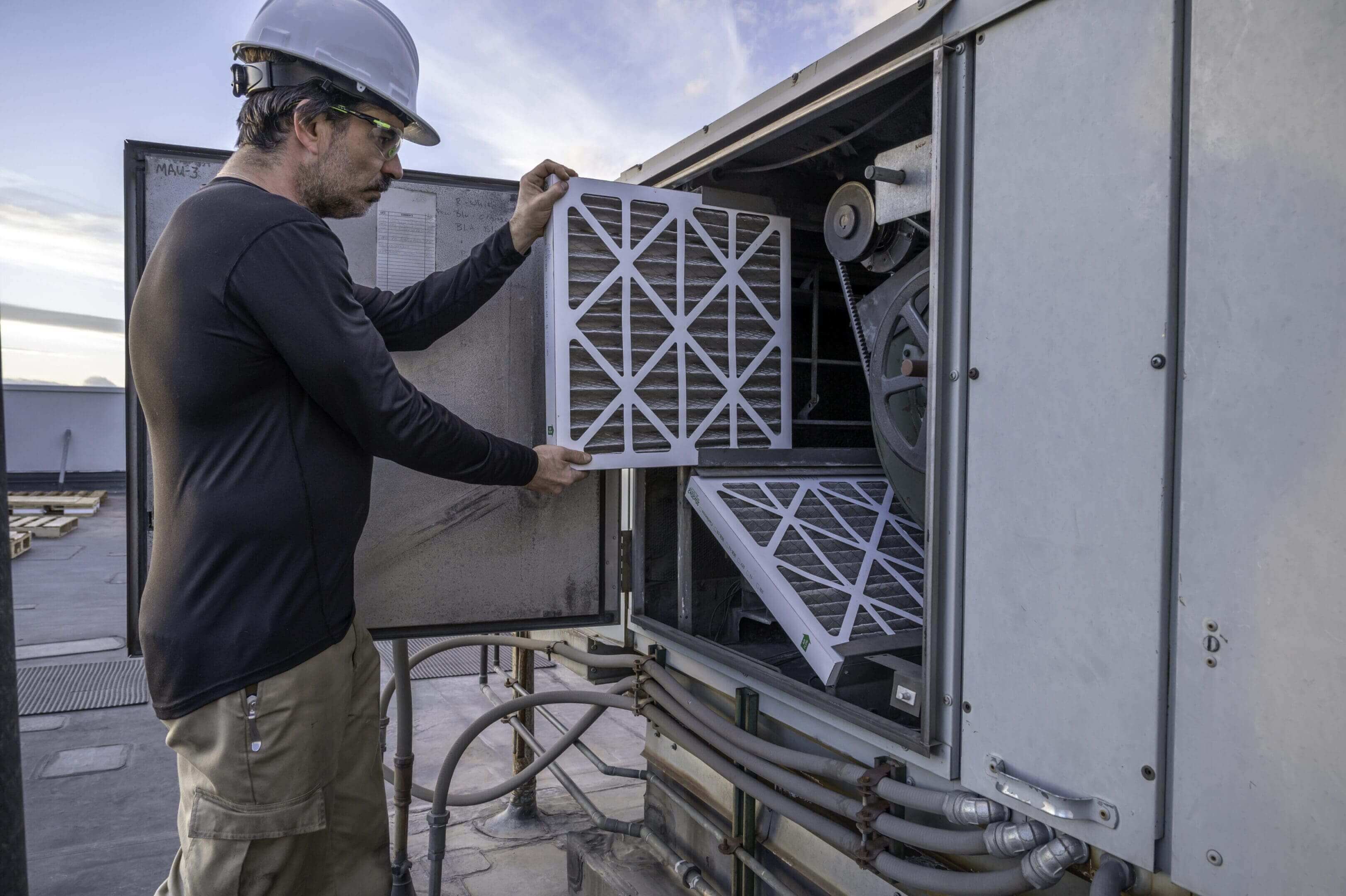 A man in hard hat and safety glasses working on air filter.